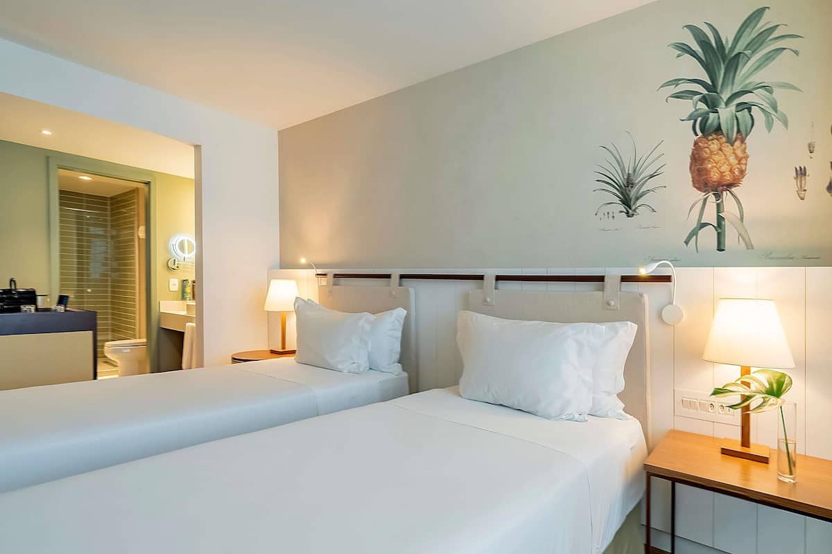 A hotel room with two beds, a bathroom, and a wall with plant illustrations.