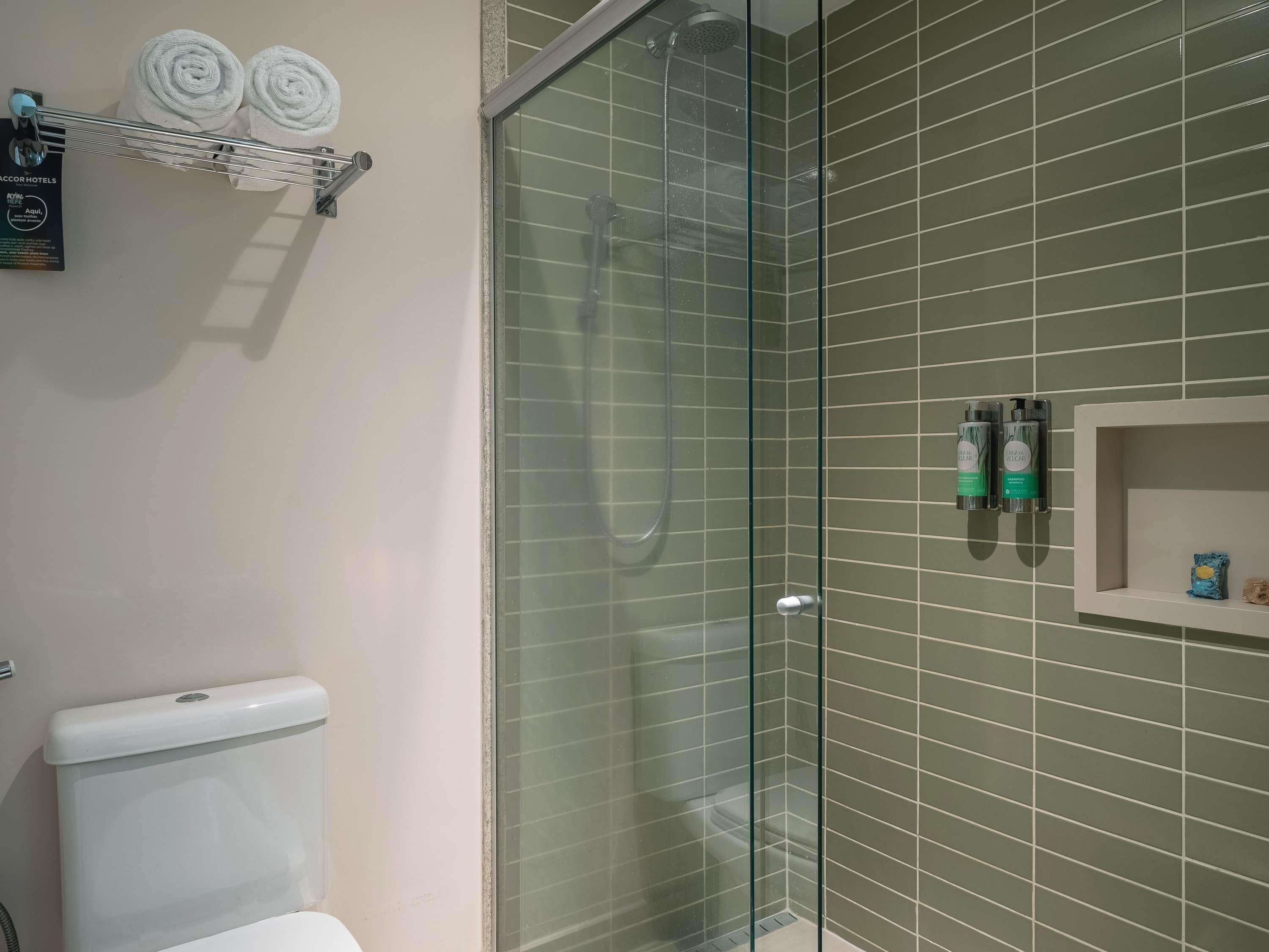 Een badkamer met een douchecabine van glas, toilet en een plank met toiletartikelen.