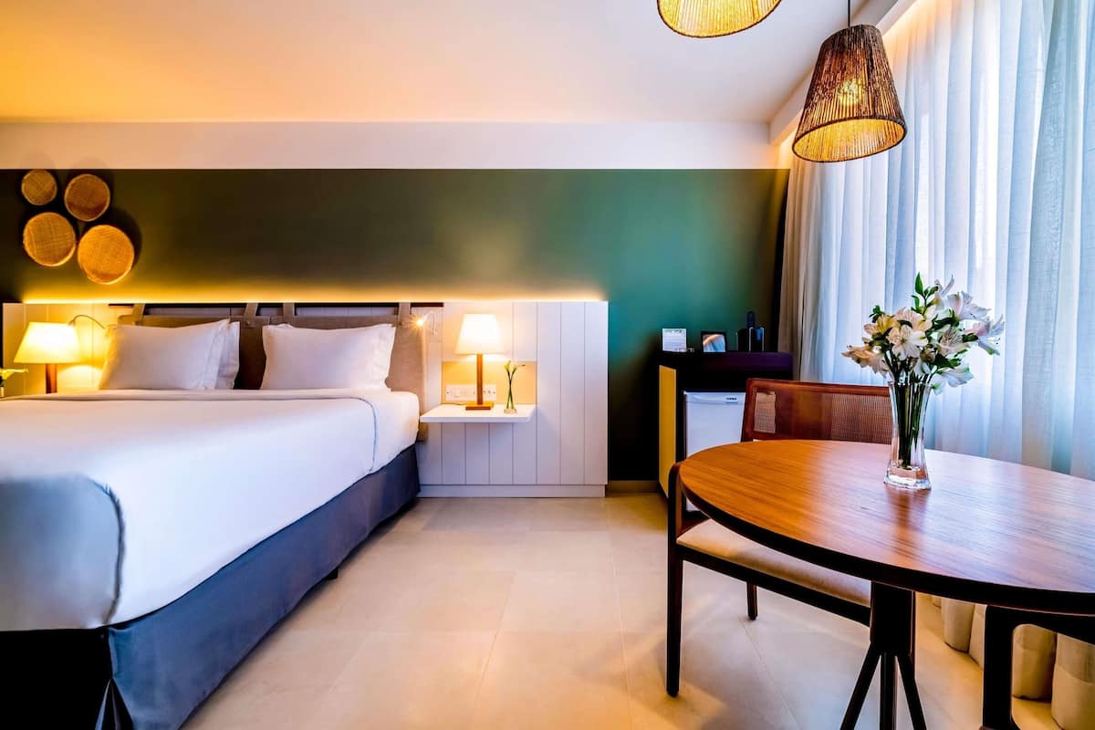 Une chambre dâhĂŽtel comprenant un lit, des tables de chevet avec des lampes, une table Ă manger avec des chaises et un vase avec des fleurs.