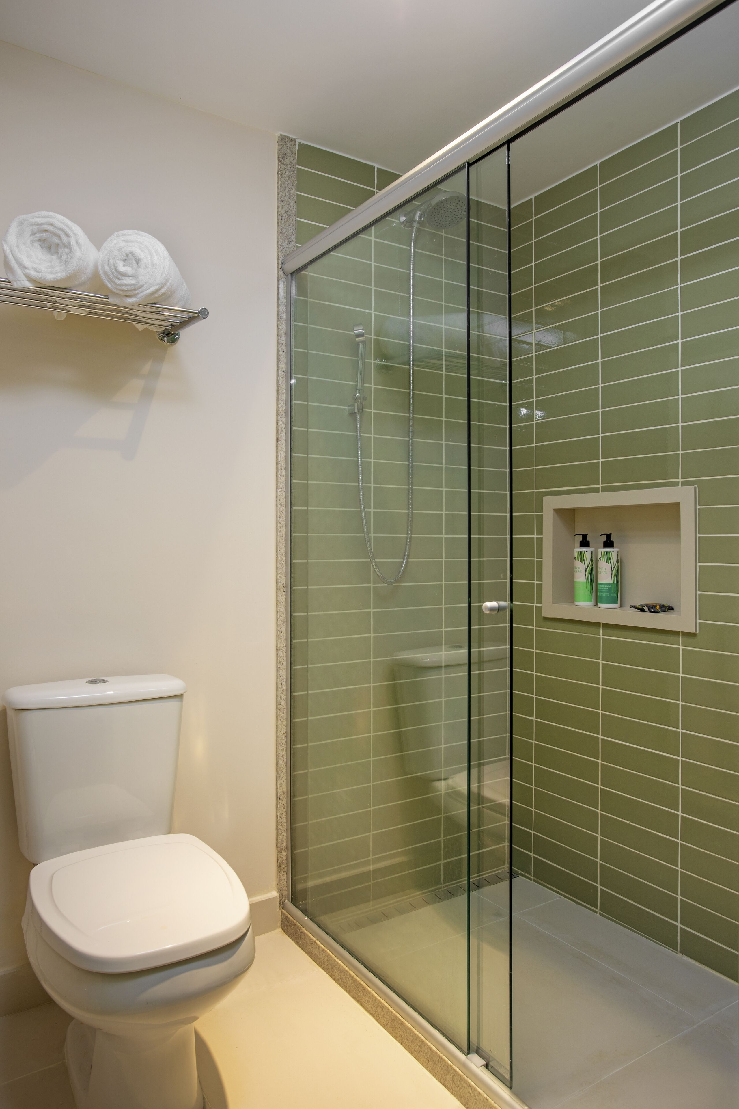 A bathroom with a glass-enclosed shower, a toilet, and a shelf with rolled towels.