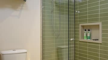 A bathroom with a glass-enclosed shower, a toilet, and a shelf with rolled towels.
