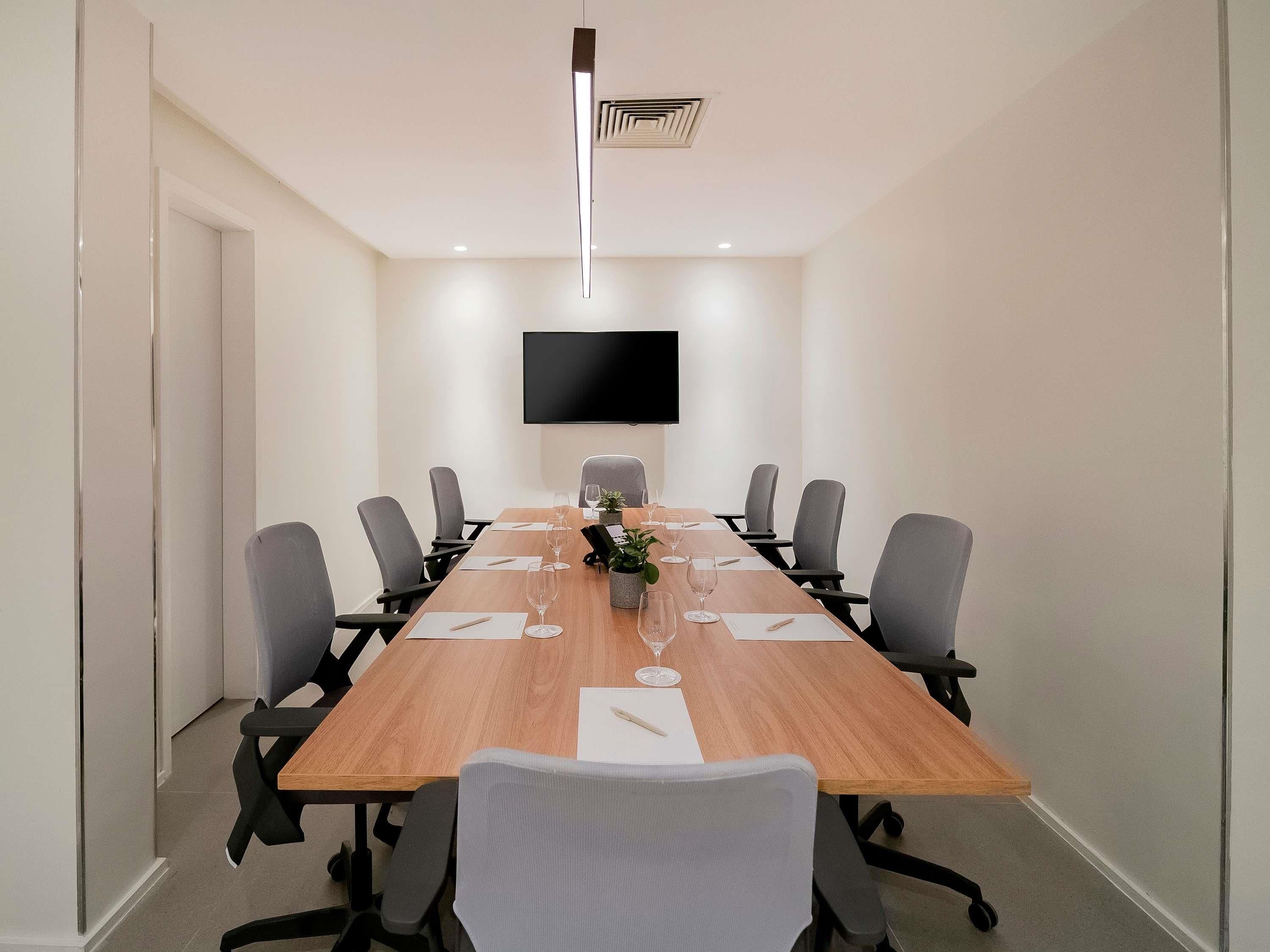 Une salle de conférence équipée d’une longue table, de chaises, d’un téléviseur à écran plat et d’un luminaire moderne au plafond.
