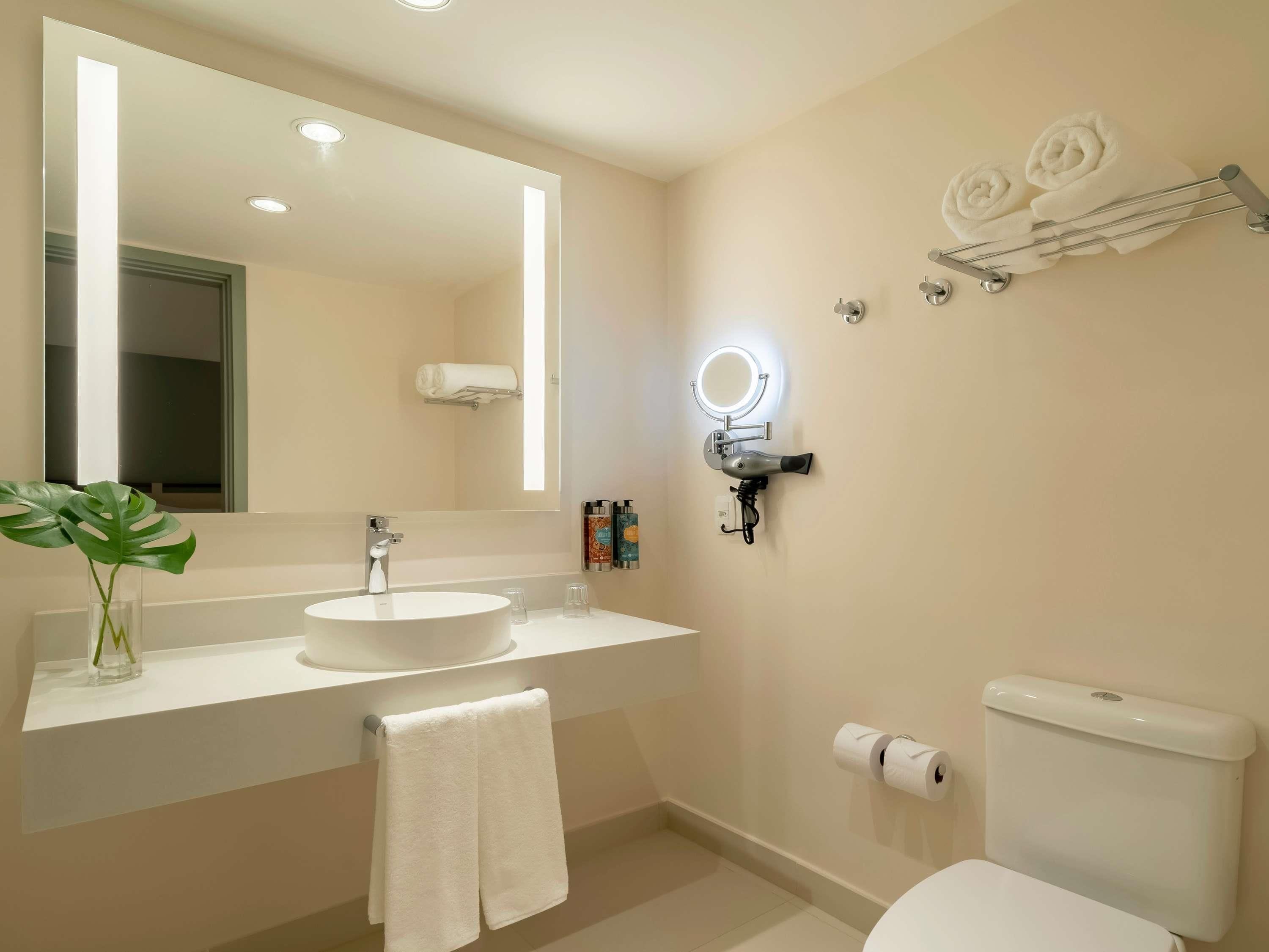 Un baño moderno con un espejo grande, un lavabo, un inodoro y un perchero para toallas.