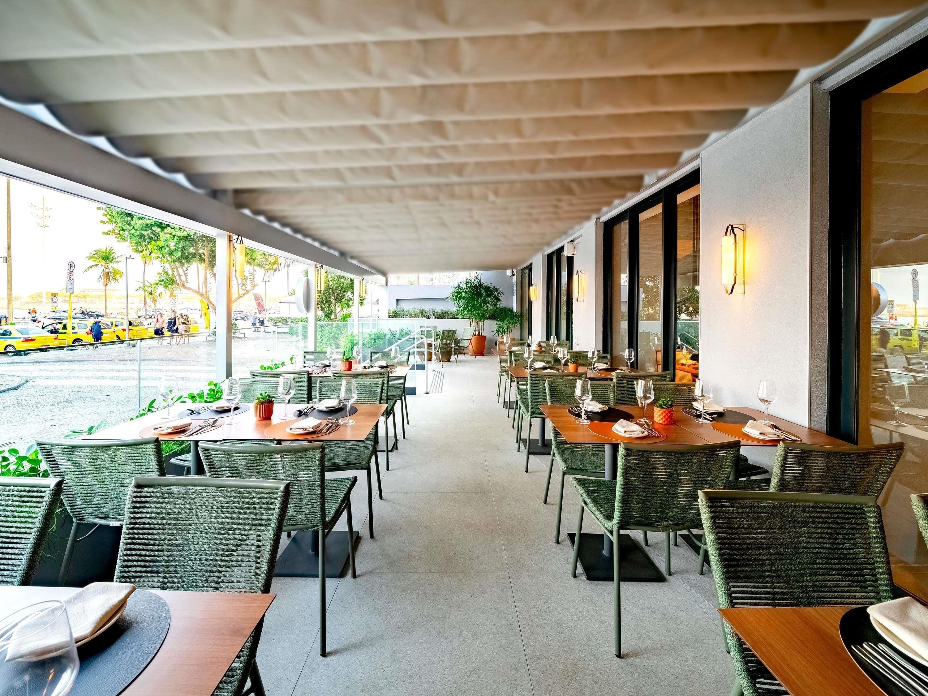 An outdoor dining area with wicker chairs and tables, large windows, and potted plants.