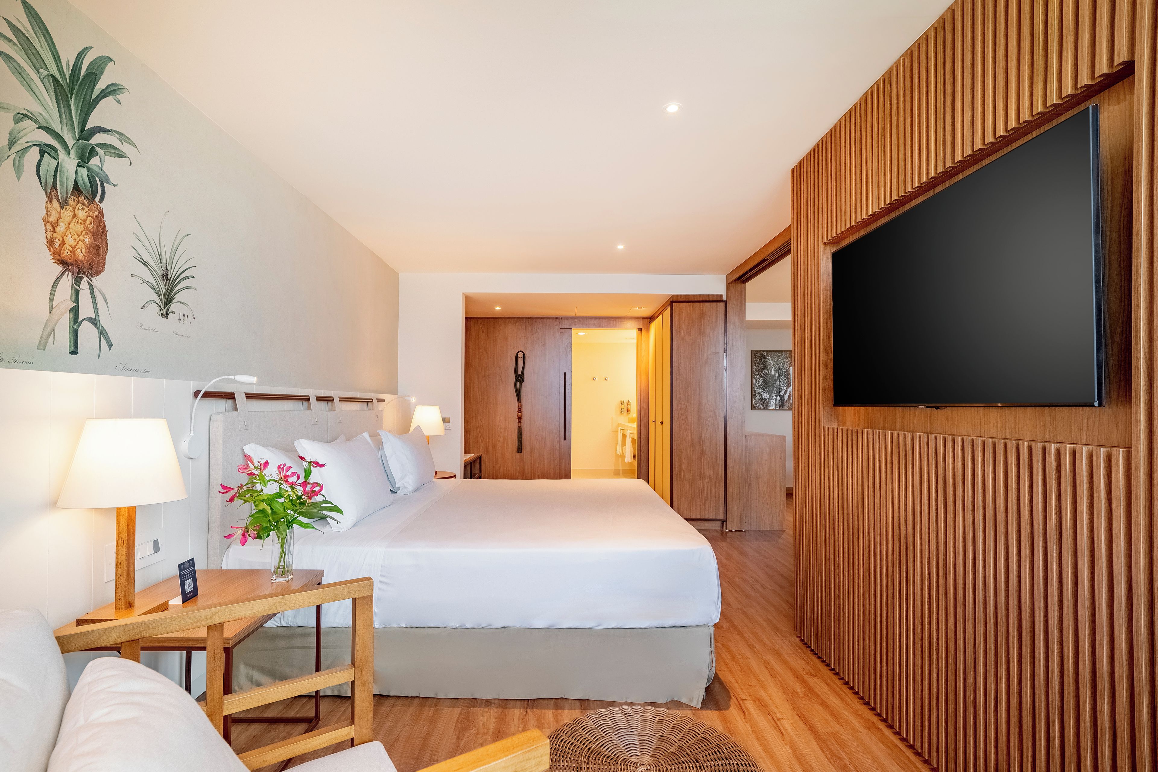 Habitación de hotel con cama, mesita de noche, lámpara y televisor de pantalla plana montado en la pared.