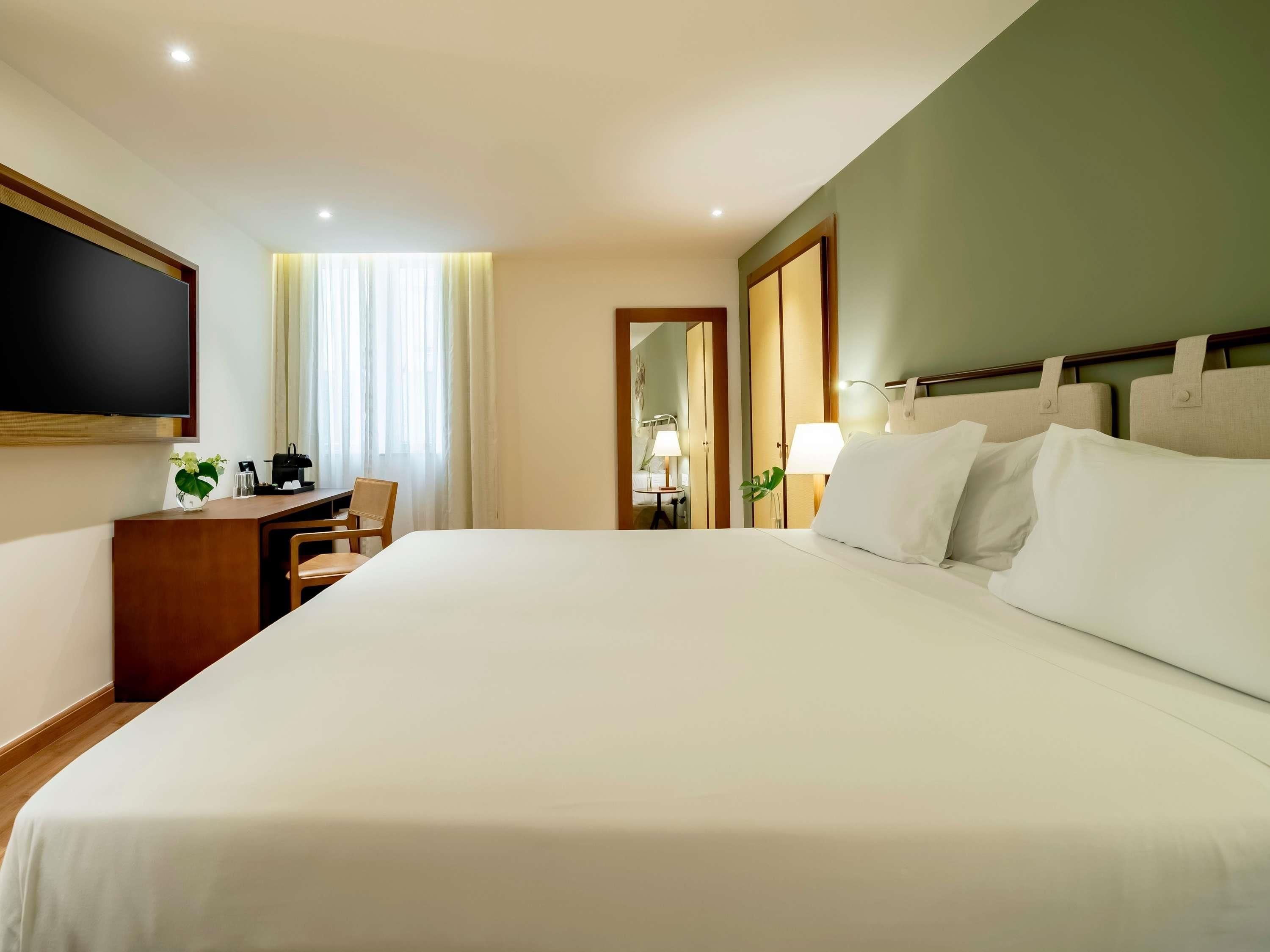 Une chambre d’hôtel avec un grand lit, un bureau avec une chaise, un téléviseur fixé au mur et un miroir.
