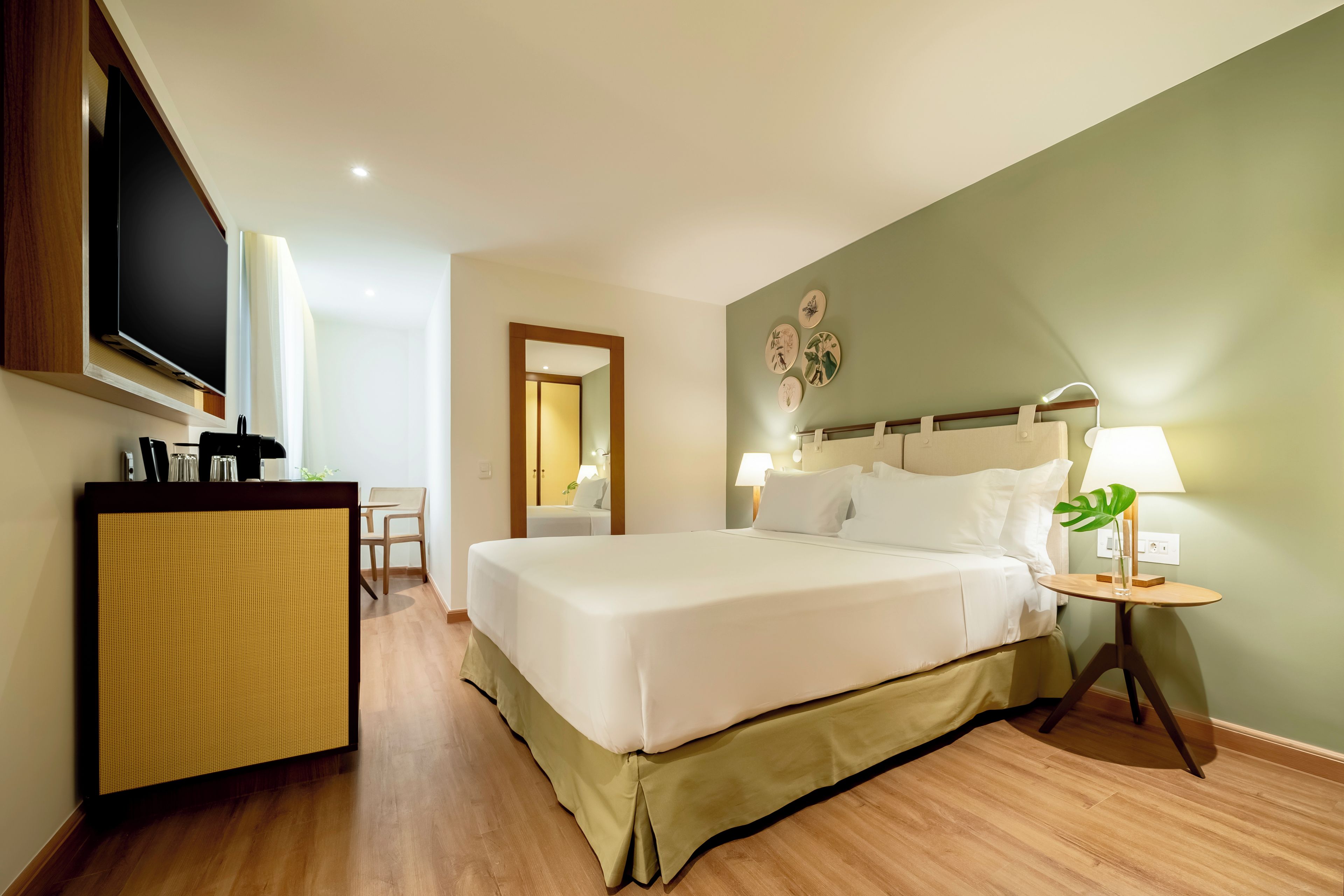 A hotel room with a bed, bedside table, lamp, and a television on a stand.