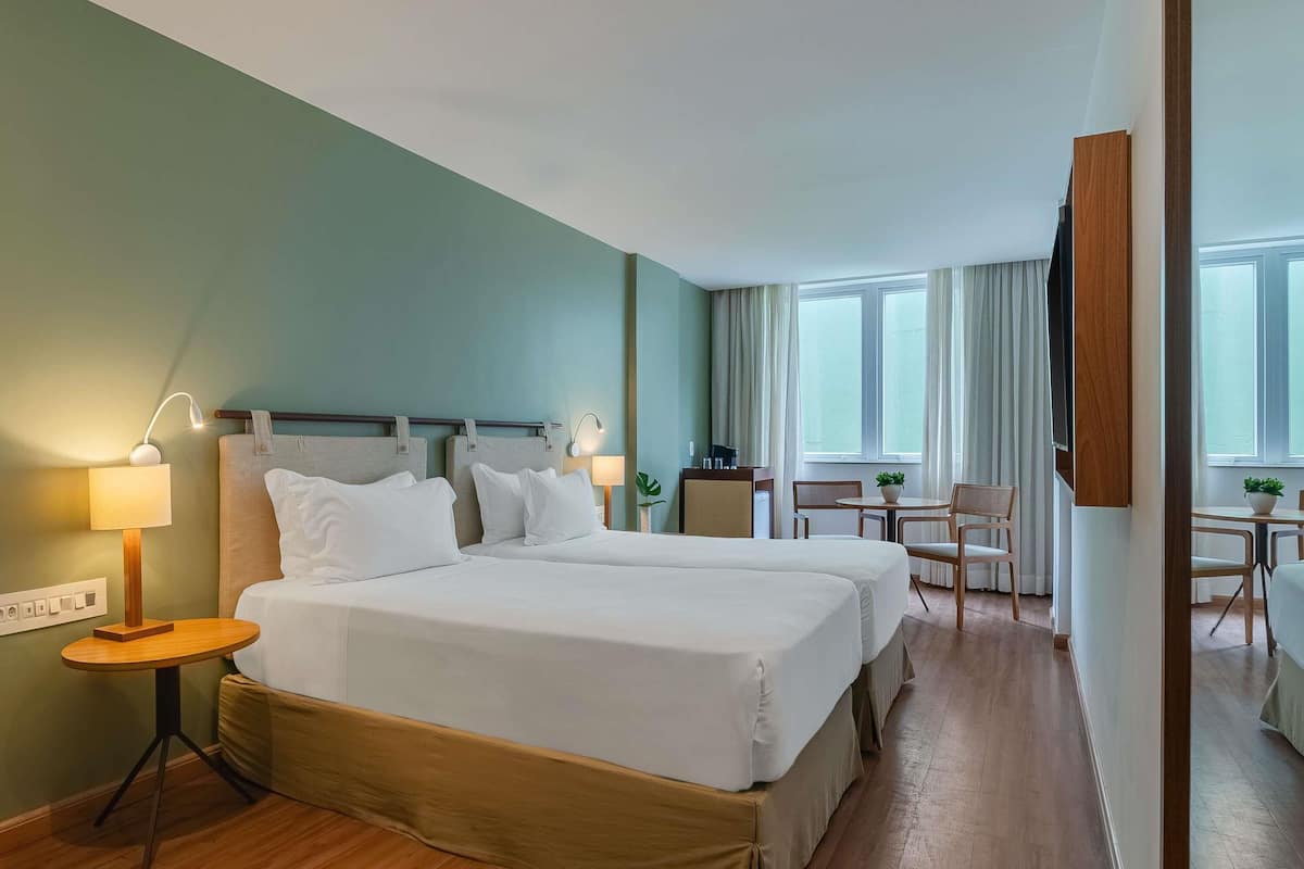 A hotel room with two beds, a desk, chairs, a small table, and a mirror.