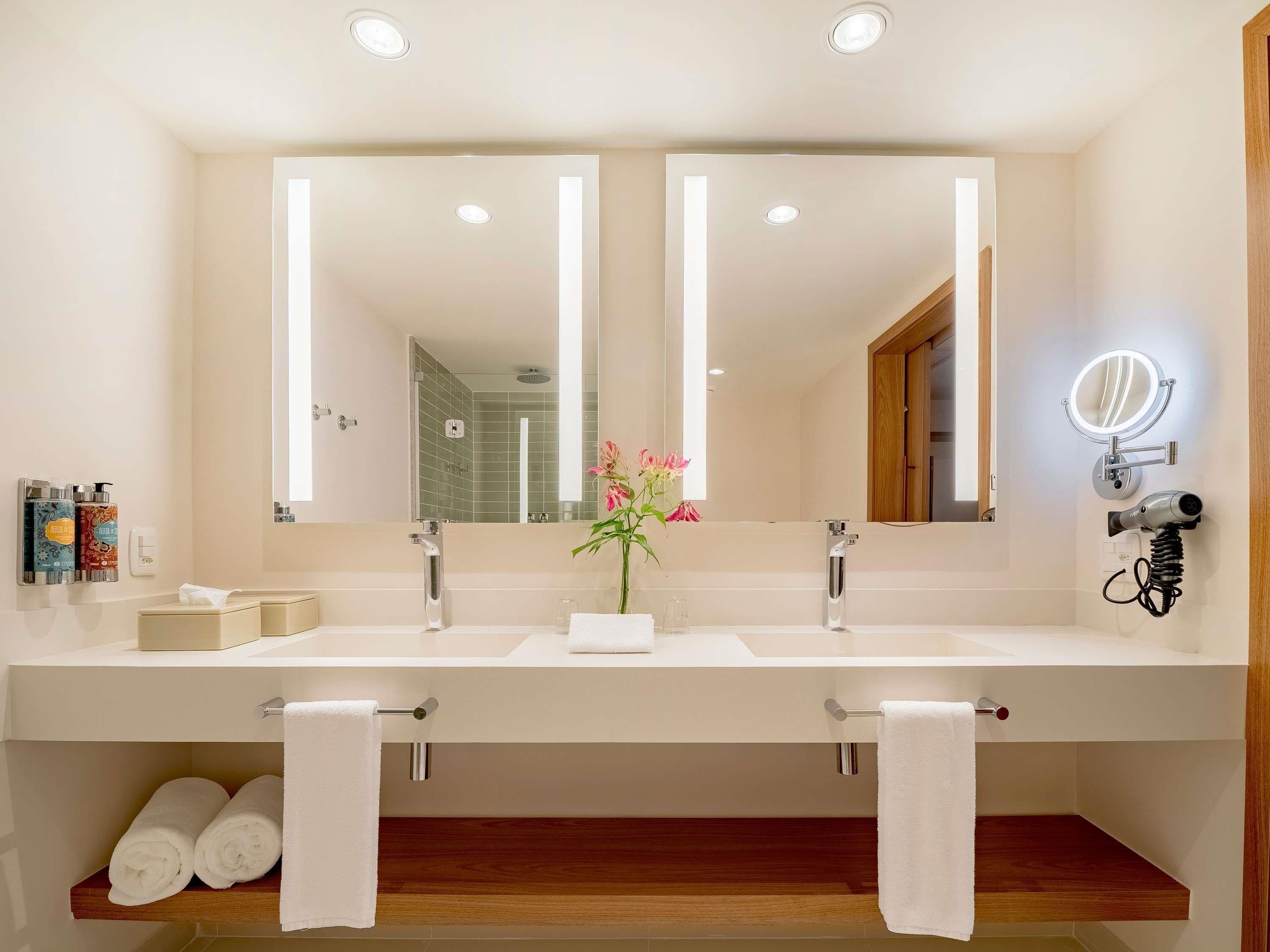 Ein Badezimmer mit zwei Waschbecken, einem großen Spiegel, einem Fön und einer Vase mit Blumen.