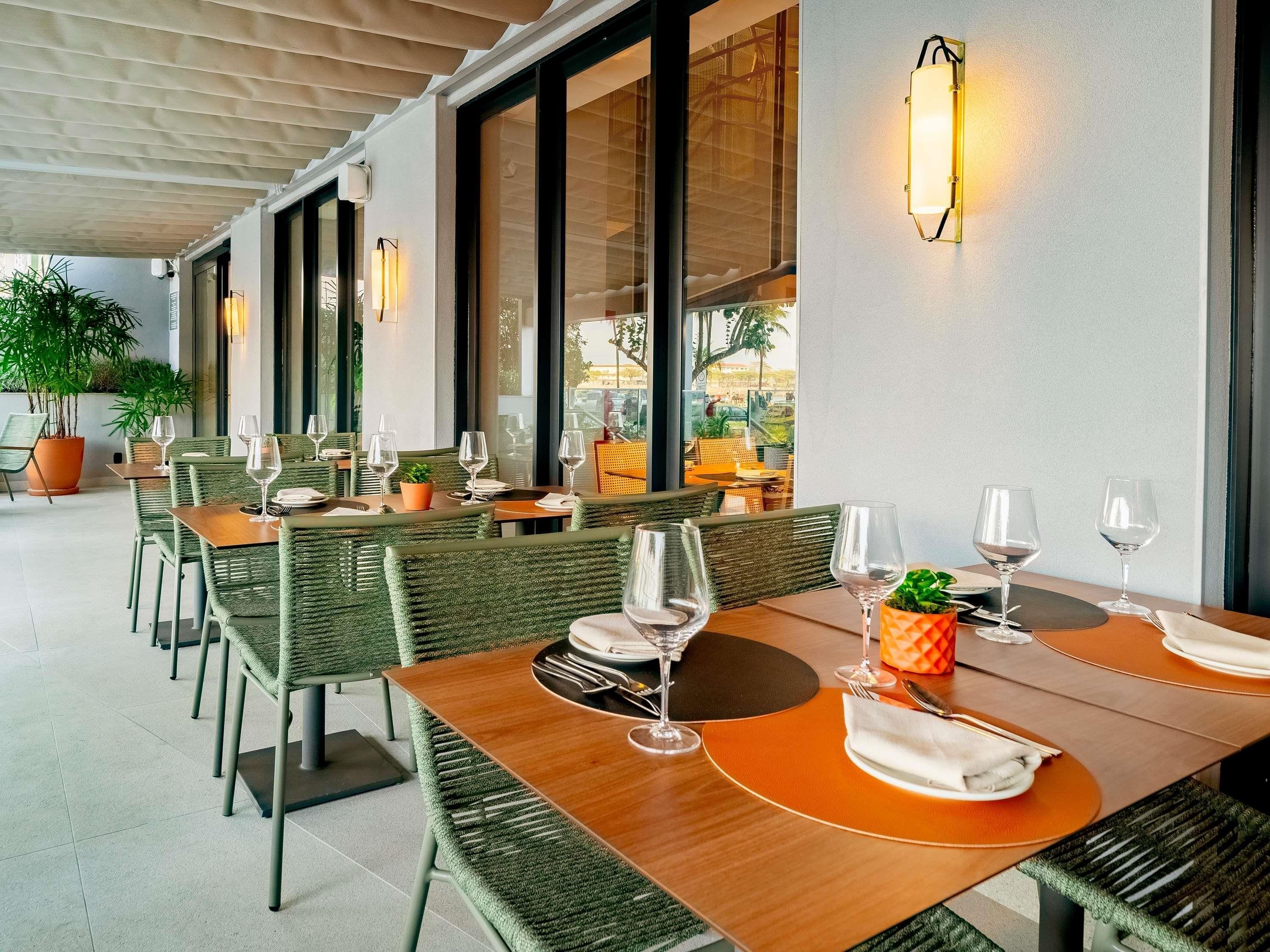 A restaurant with outdoor seating, tables with chairs, potted plants, and wall-mounted lighting.
