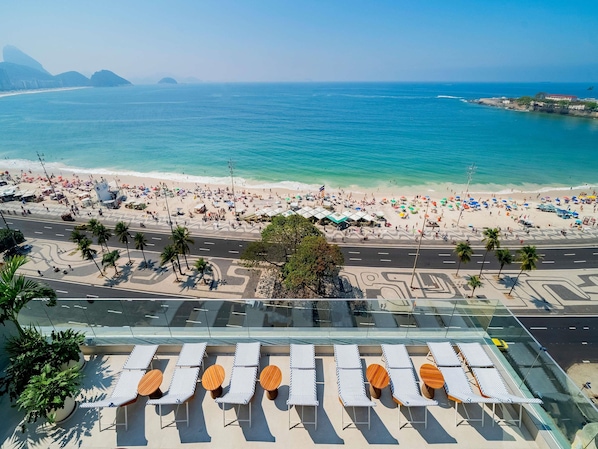 A beachside hotel with outdoor seating, a view of the beach, and a road in the foreground. - Grand Mercure Rio de Janeiro Copacabana (Rio de Janeiro)