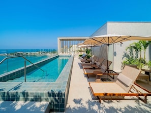 A rooftop pool area with a clear view of the ocean, lounge chairs, and umbrellas. - Grand Mercure Rio de Janeiro Copacabana (Rio de Janeiro)