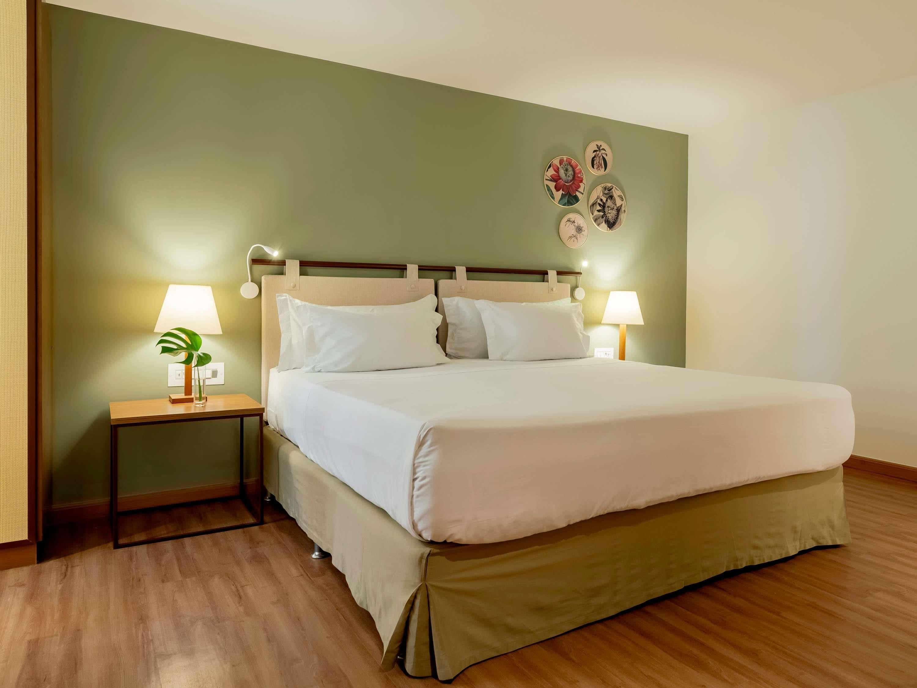A neatly made bed with white linens, two bedside tables with lamps, a small plant on one table, and a wall with four decorative plates.