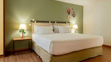 A neatly made bed with white linens, two bedside tables with lamps, a small plant on one table, and a wall with four decorative plates.