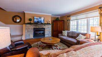 A cozy living room with a stone fireplace, leather sofas, a round coffee table, and a television mounted above the fireplace.