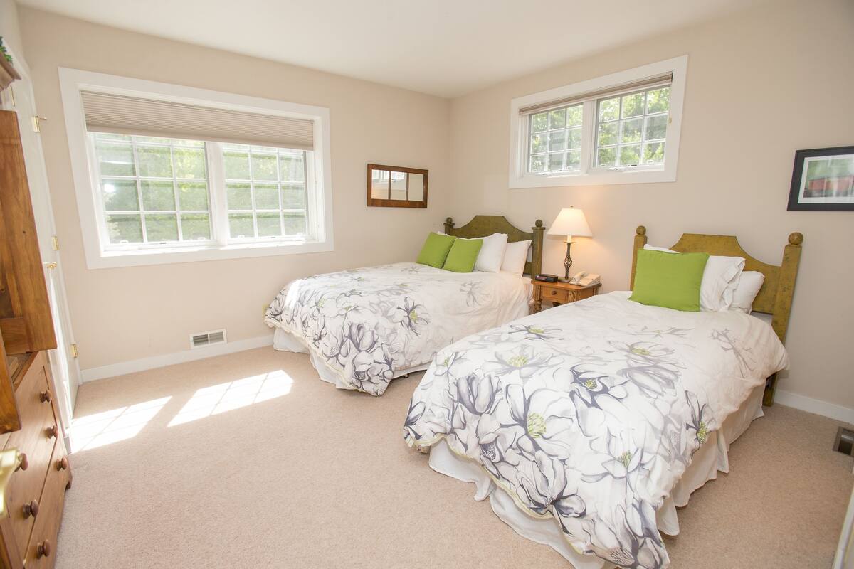 A bedroom with two beds, each with floral bedding, a nightstand with a lamp, and a window with blinds.