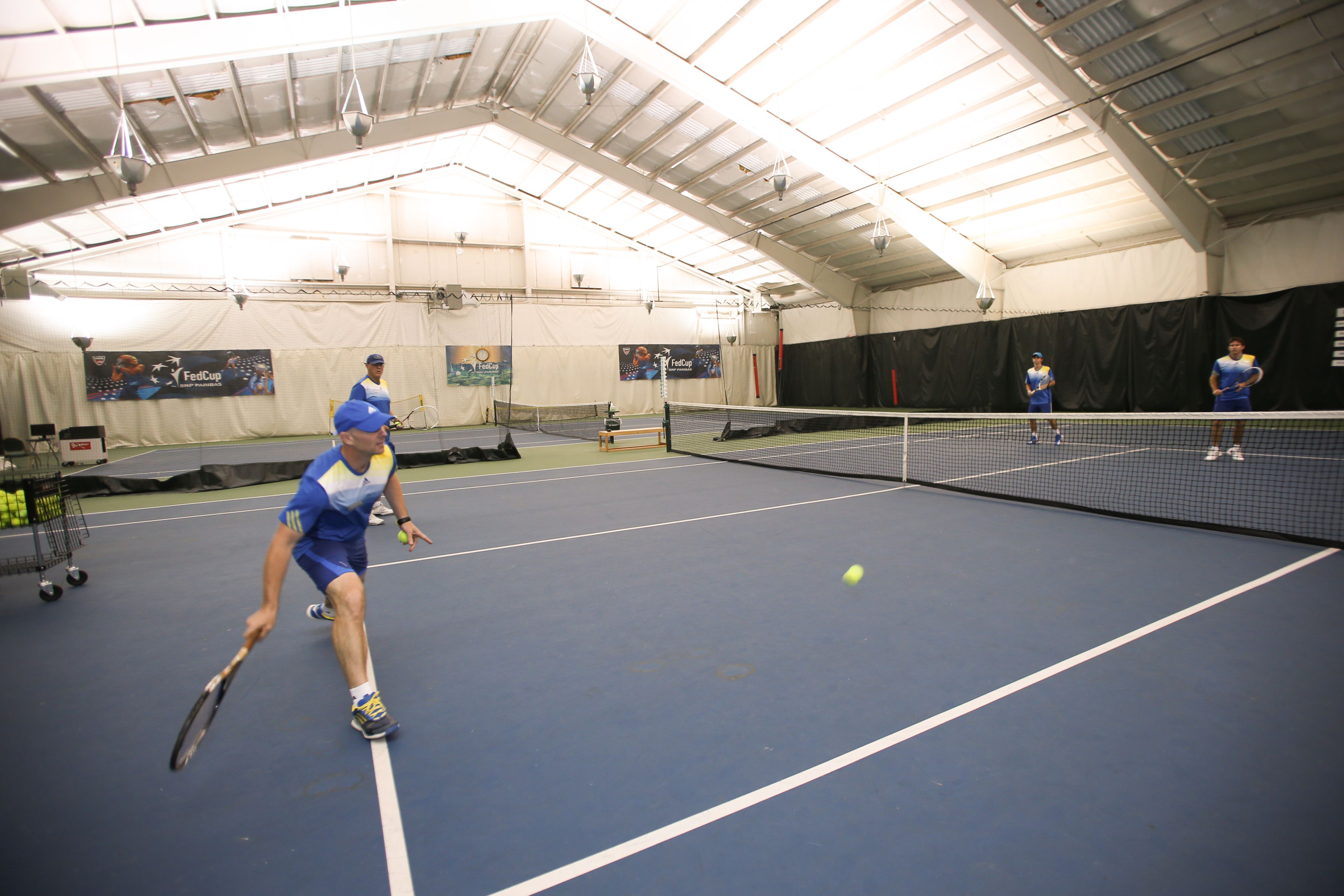 Una corte da tennis al chiuso con una rete, un giocatore in blu e un altro giocatore sullo sfondo.