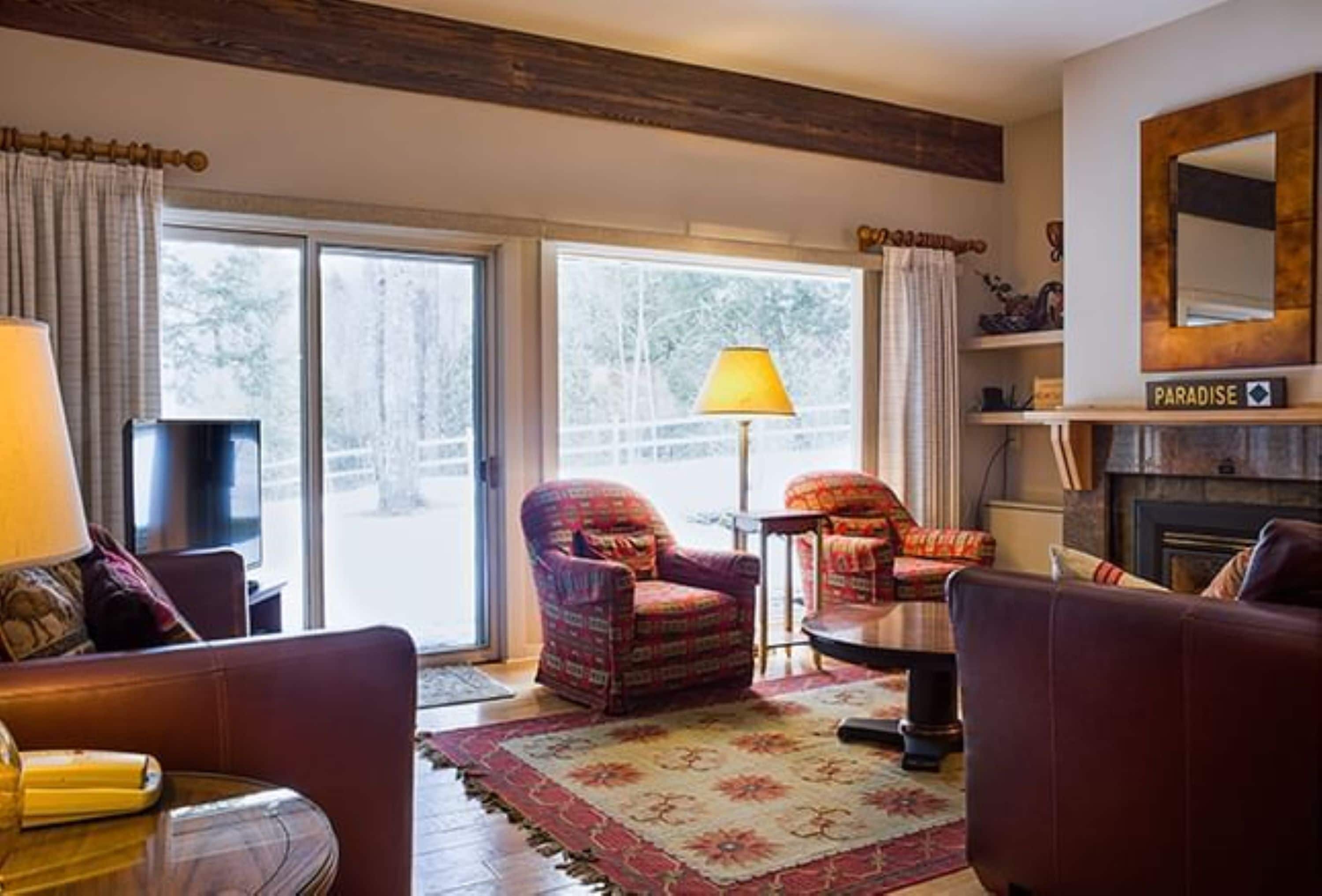 A cozy living room with a fireplace, a large window, and a sofa.