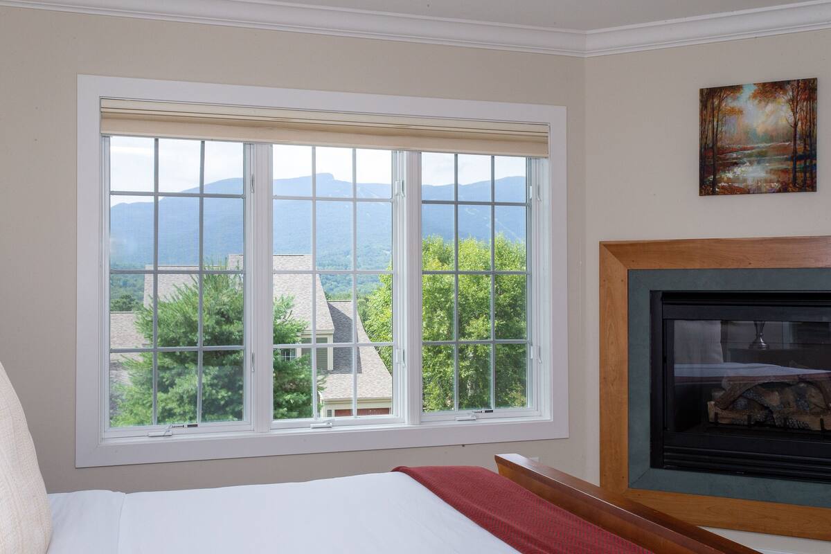 A bedroom with a large window offering a view of mountains and trees.