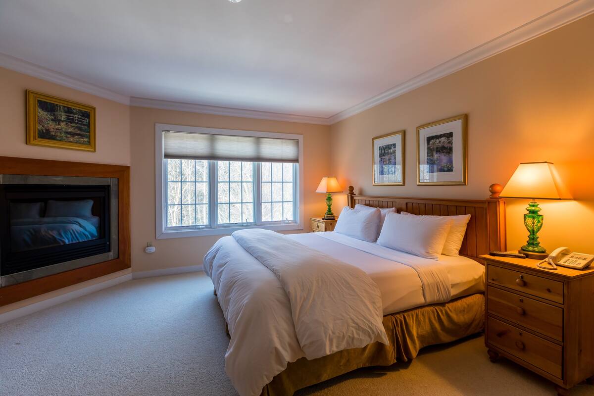 A neatly arranged bedroom with a large bed, bedside lamps, a nightstand, and a fireplace.