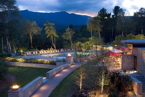 A pool area with lounge chairs and a fire feature, surrounded by a landscaped garden and a building with a stone facade. - Topnotch Resort (Stowe)