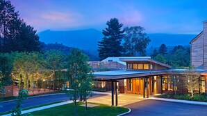 Un hotel moderno con entrada cubierta, rodeado de árboles y vistas a montañas.
