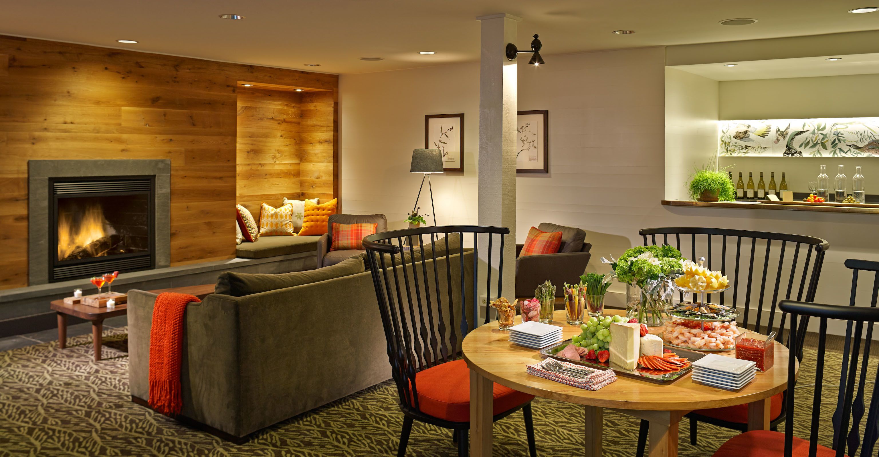 A cozy living room with a fireplace, comfortable seating, and a dining area with a variety of food and drinks.