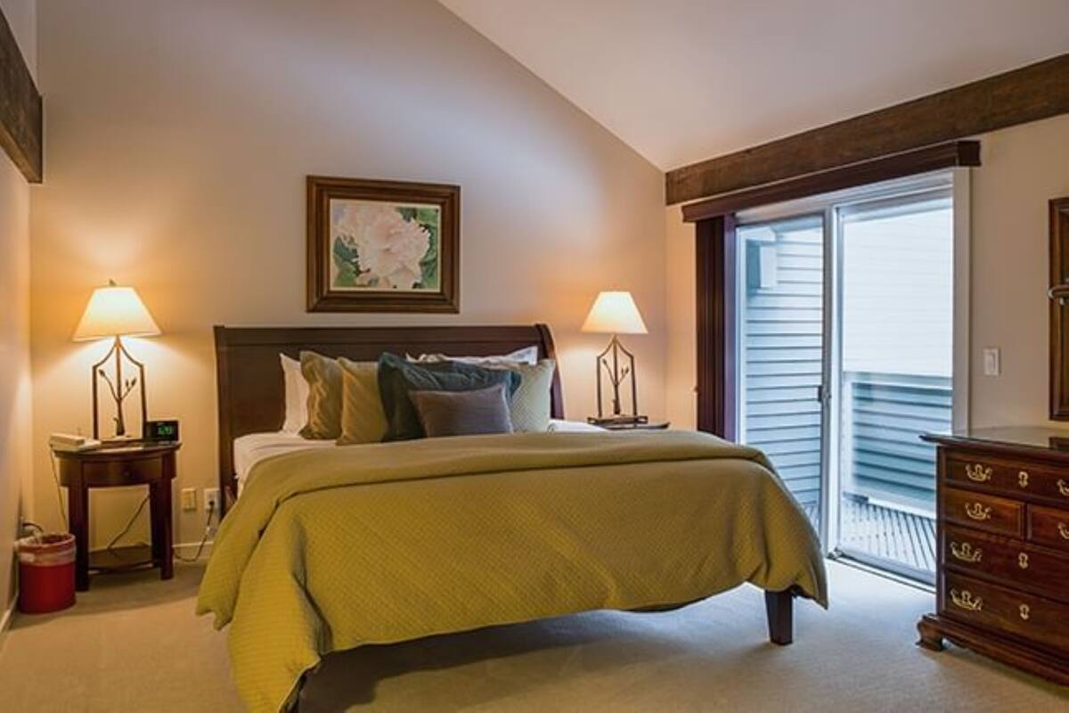 A bedroom with a bed, two bedside tables with lamps, a dresser, and a sliding glass door to the outside.