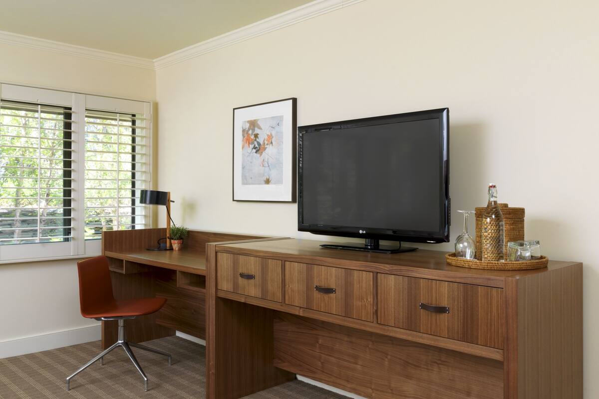 A modern office space with a wooden desk, a chair, a television, and a framed artwork on the wall.