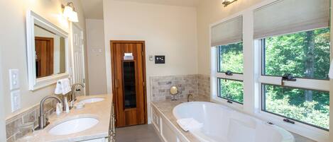 Un baño moderno con dos lavabos, una bañera grande y vistas al exterior a través de amplios ventanales.