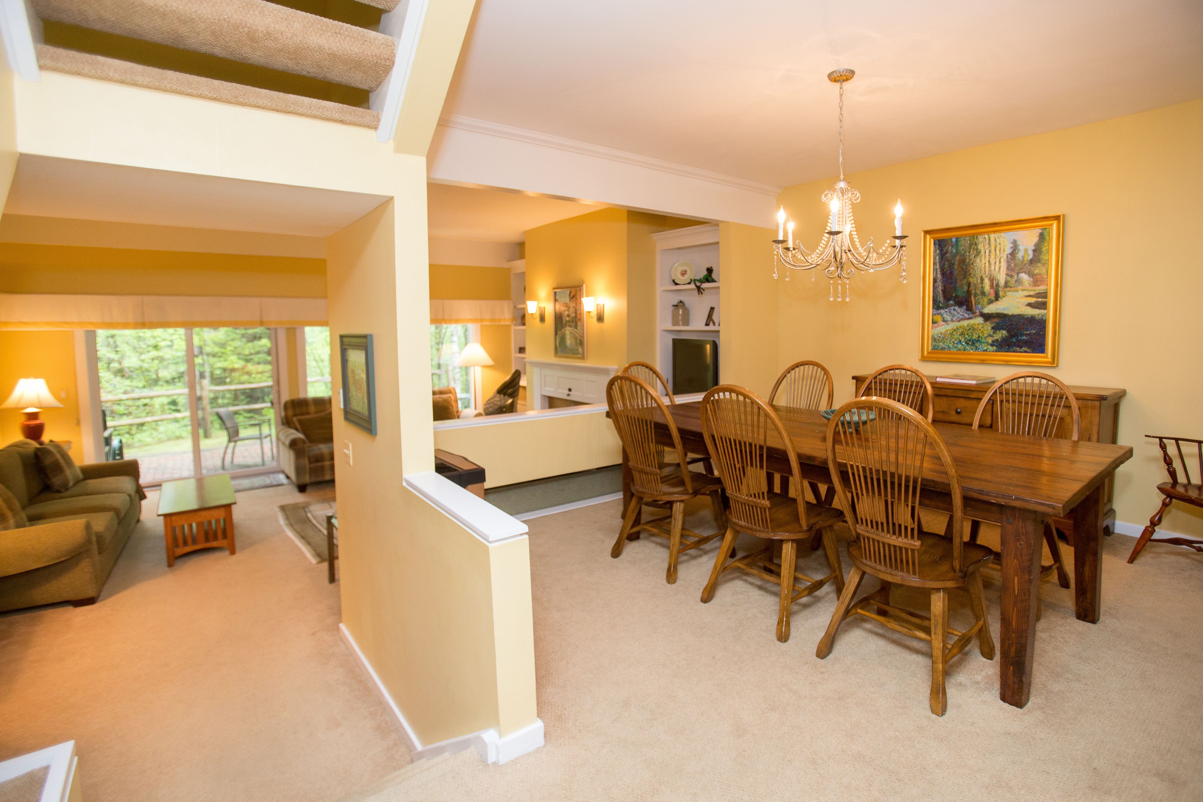 A spacious dining area with a wooden table and chairs, a chandelier, and a painting on the wall.