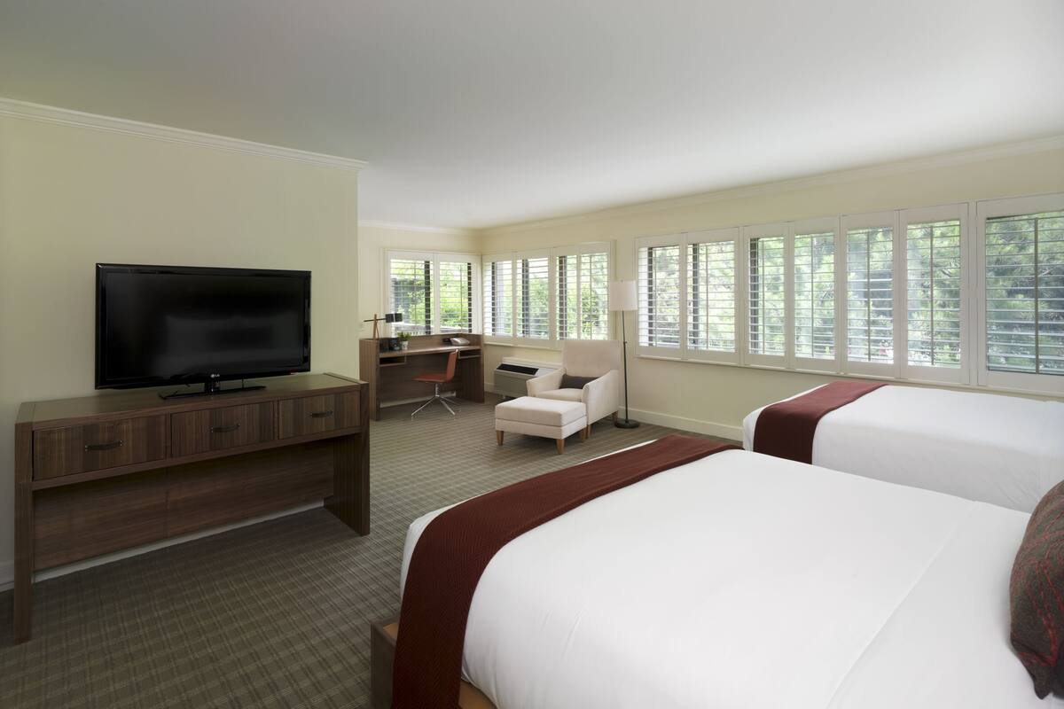A hotel room with a TV, a desk, two chairs, and large windows.