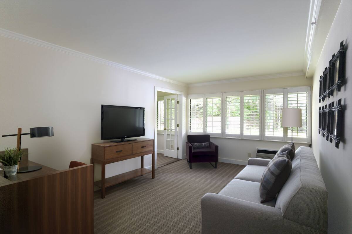 A living room with a TV on a wooden stand, a sofa, a chair, and a lamp.