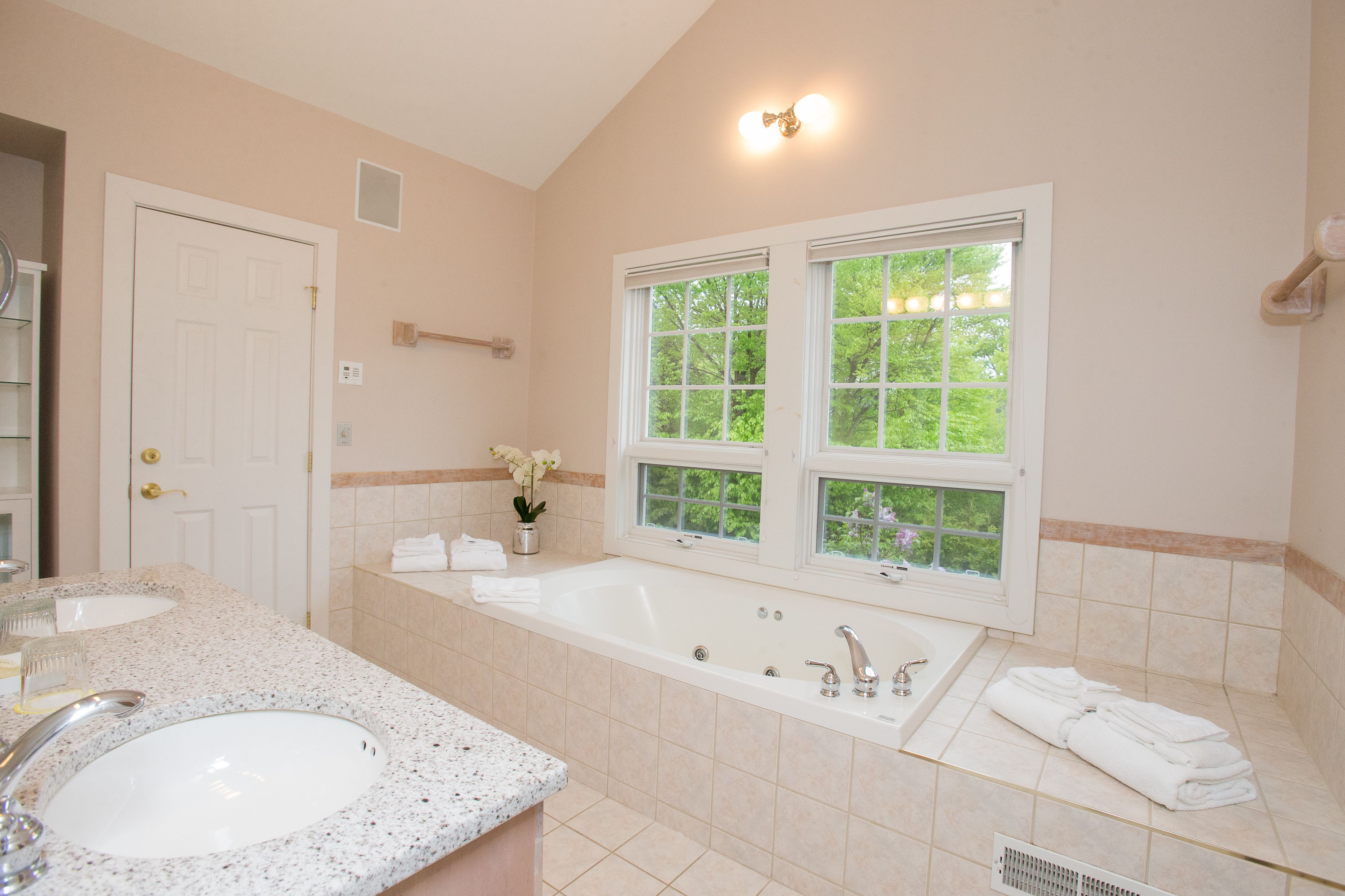 A bathroom with a large bathtub, a sink, and a window with a view of trees.
