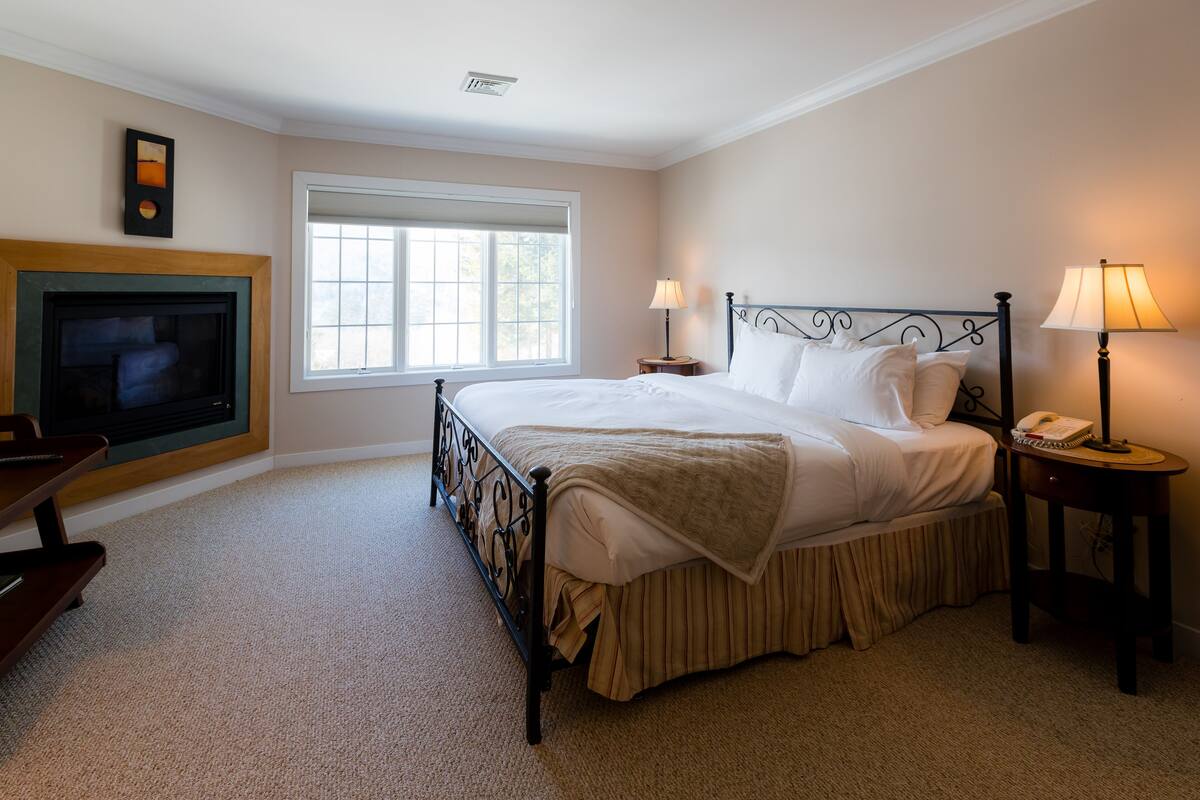A bedroom with a bed, two bedside lamps, a nightstand, a TV, and a window.