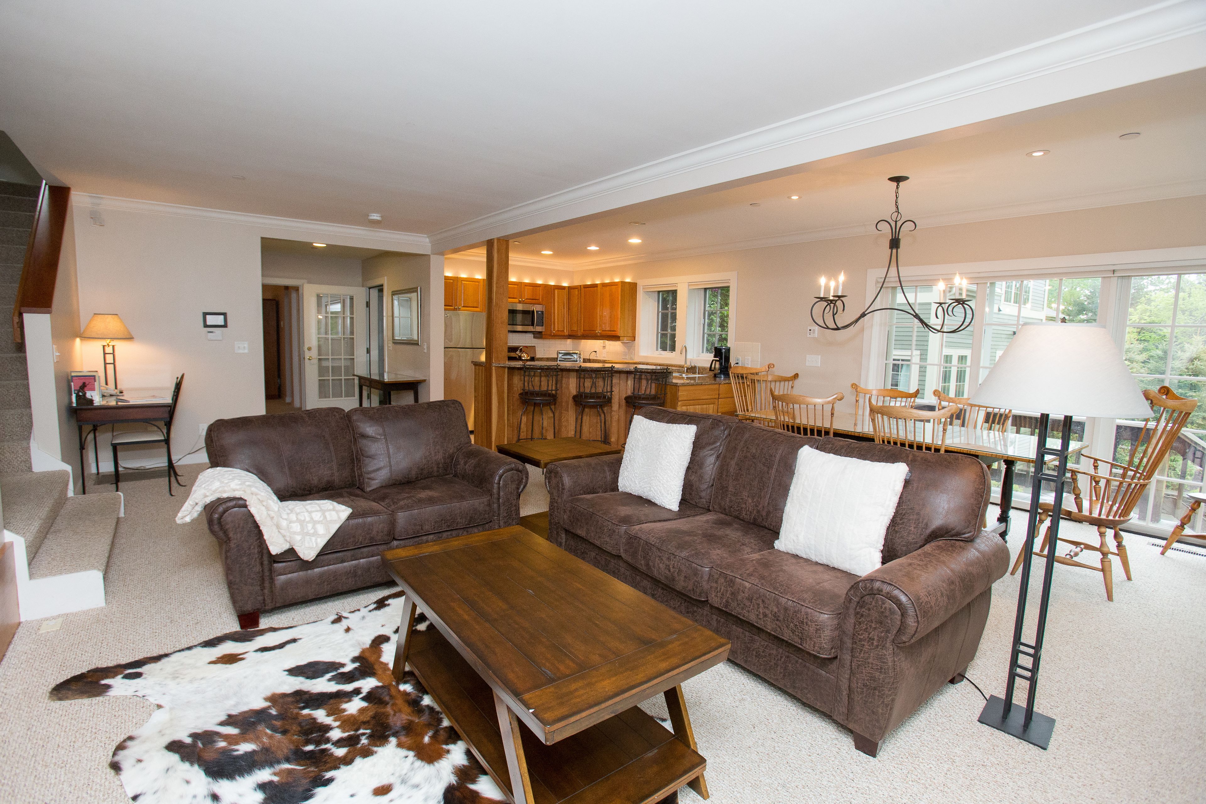 A spacious living room with two brown leather sofas, a wooden coffee table, and a large rug.