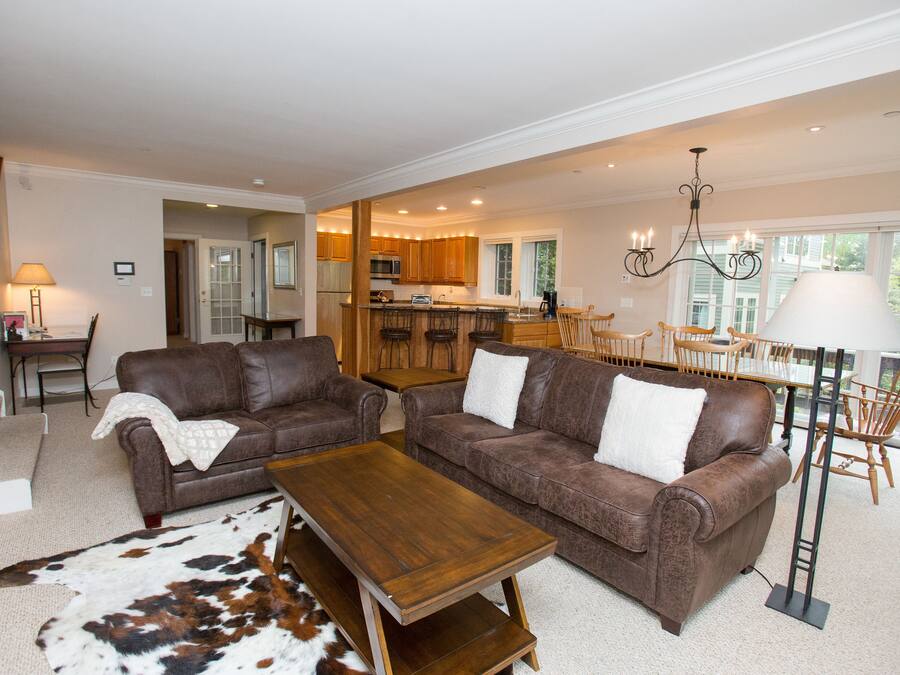 A spacious living room with two brown leather sofas, a wooden coffee table, and a large rug.
