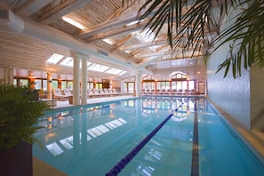 An indoor swimming pool with clear water, wooden ceiling beams, and lounge chairs along the poolside.