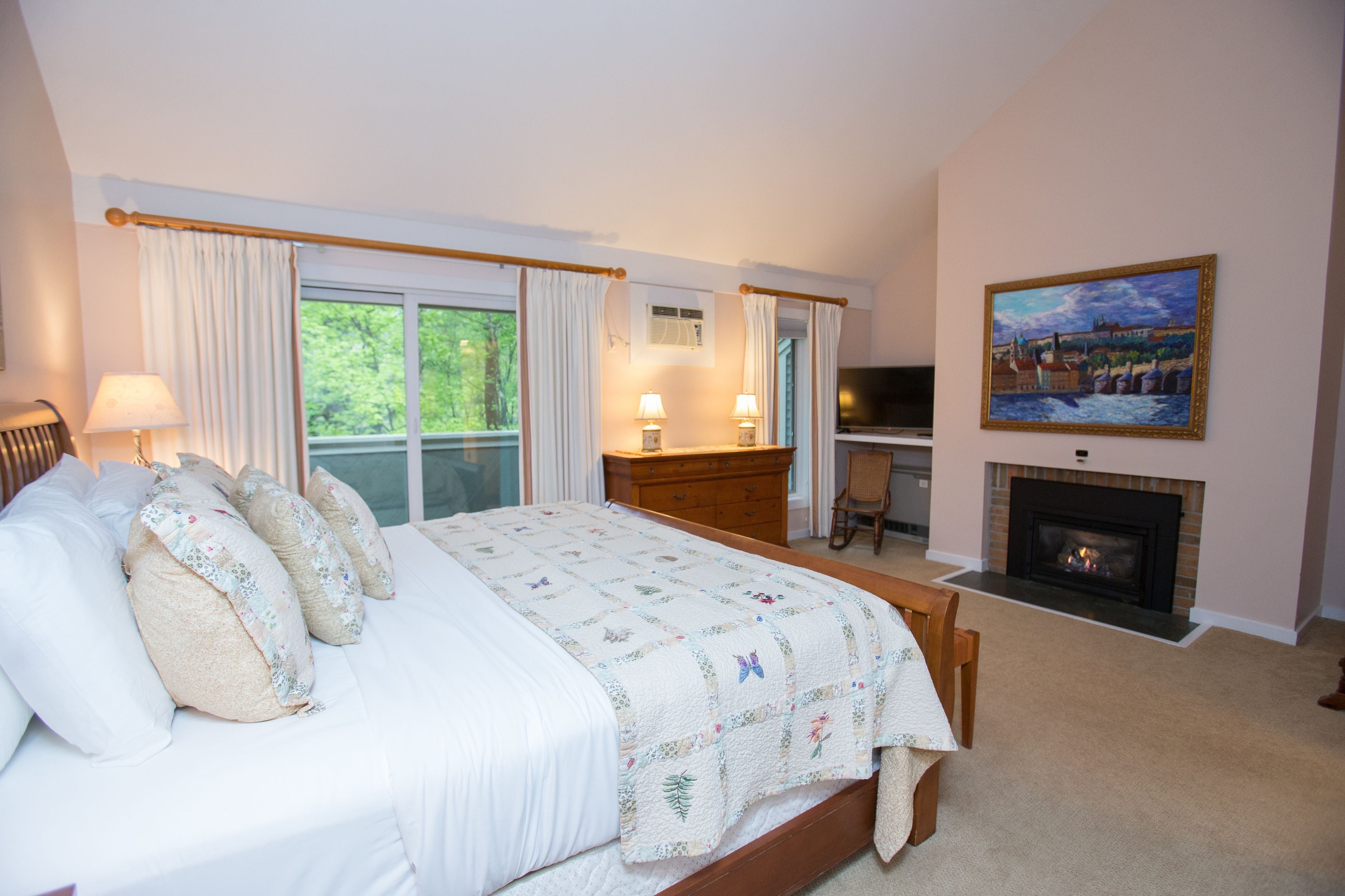 Un dormitorio con cama, cómoda, televisor, chimenea y un cuadro en la pared.