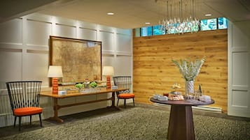 A conference room with a wooden wall, a large map, two chairs with orange cushions, a round table with a vase of flowers, and a chandelier.