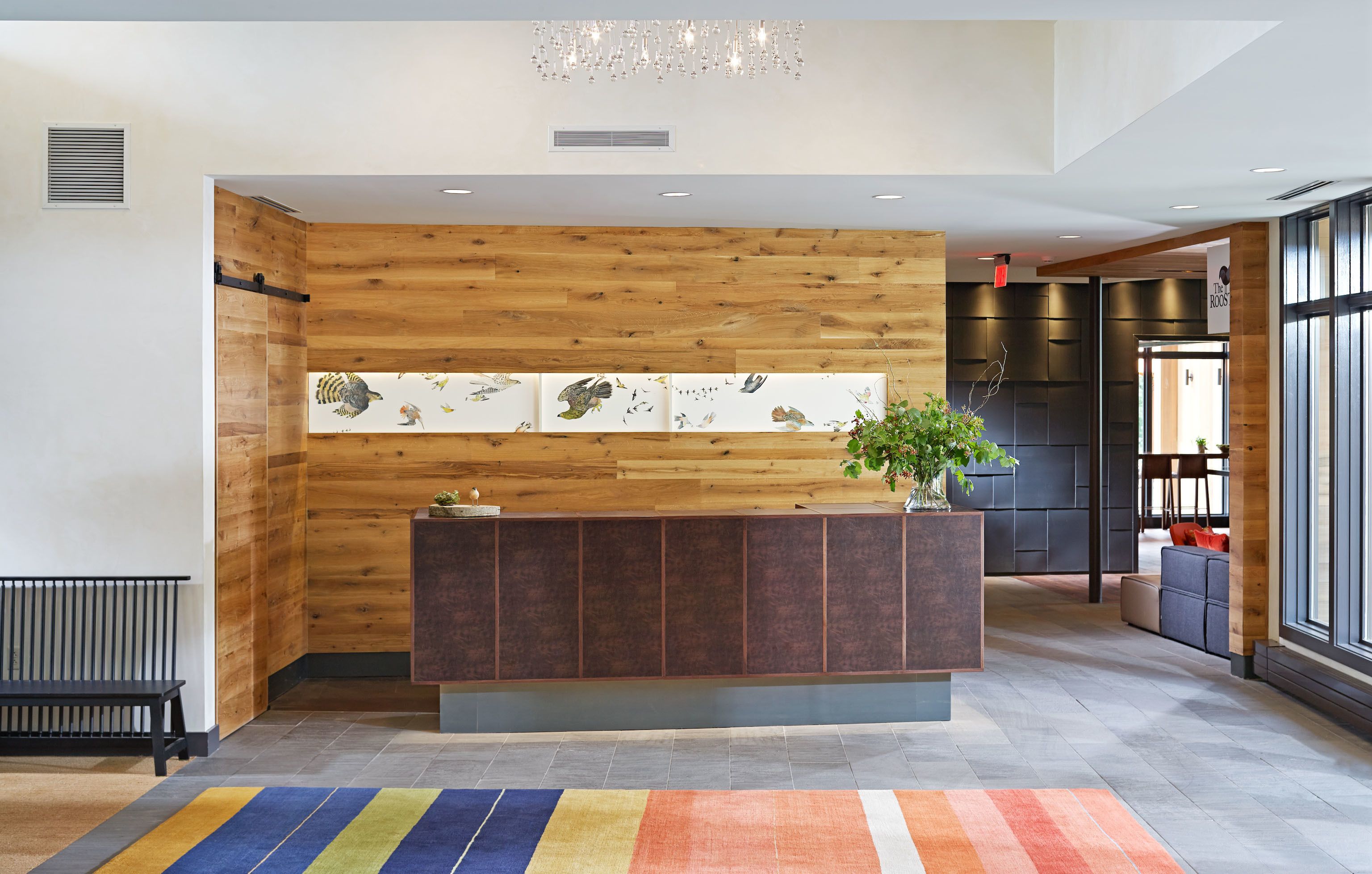 Un espace d’accueil avec un comptoir de réception en bois, un tapis aux couleurs vives et un mur orné de tableaux encadrés.