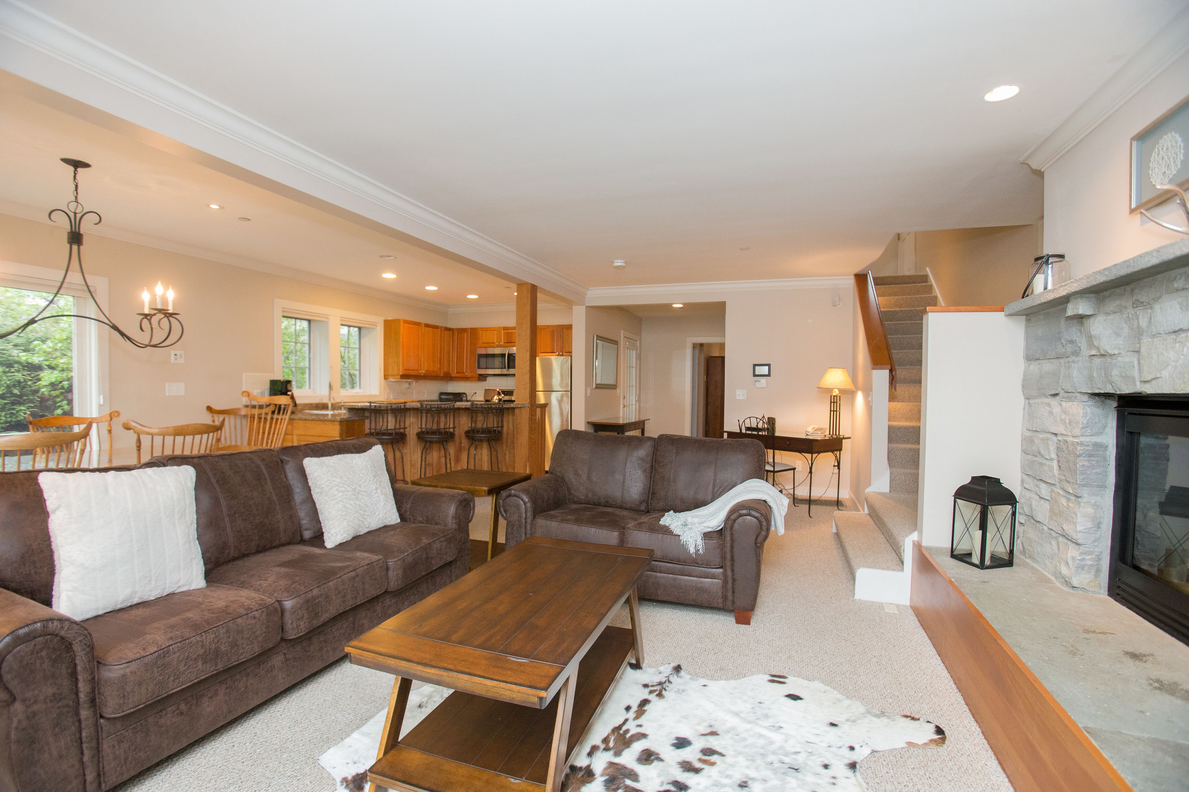 A spacious living room with a brown leather sofa, a wooden coffee table, and a stone fireplace.