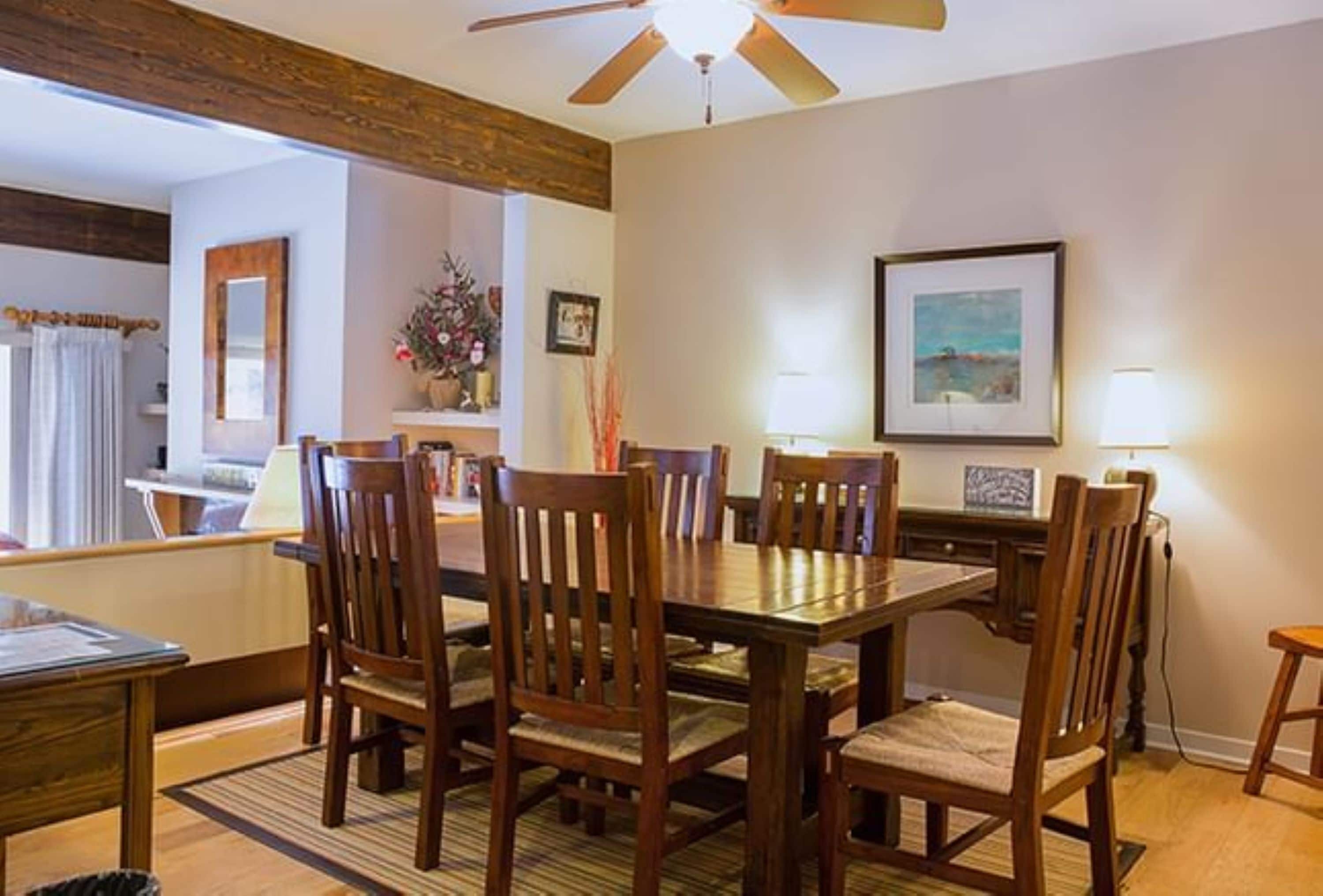 A dining area with a wooden table and chairs, a ceiling fan, and a framed picture on the wall.