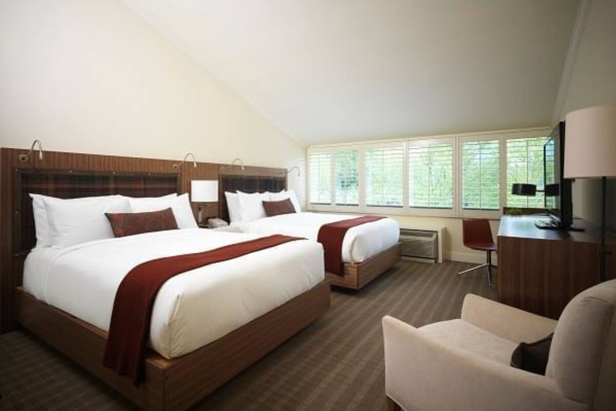 A hotel room with two beds, a desk, and a chair.