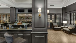 A bar area with stools, a bar counter, and a variety of bottles. There are two seating areas with chairs and tables, and a large pillar with a light fixture.