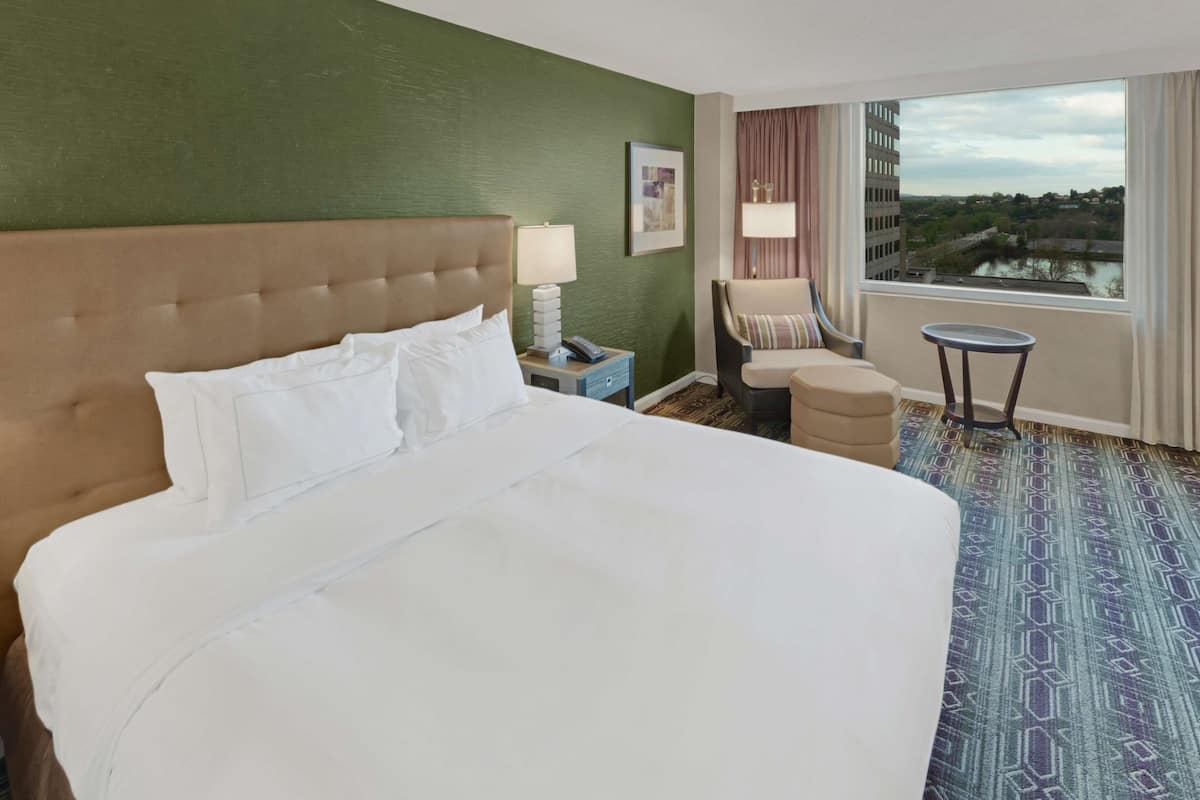 A hotel room with a large bed, a chair, a small table, and a view of a body of water through the window.