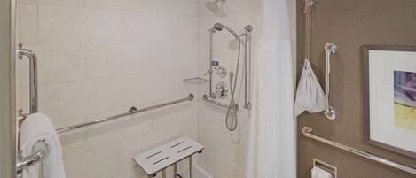 A modern bathroom with a shower, grab bars, a towel rack, and a toilet paper holder.