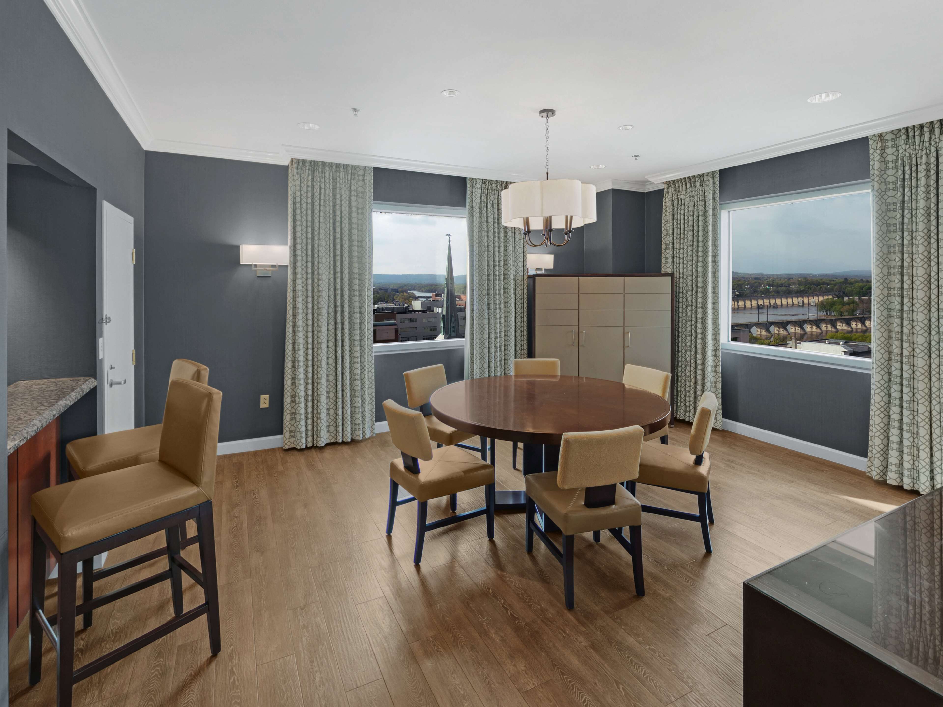 A modern dining room with a round table, six chairs, and a view of a cityscape through large windows.