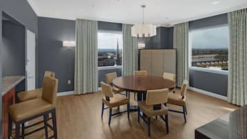 A modern dining room with a round table, six chairs, and a view of a cityscape through large windows.