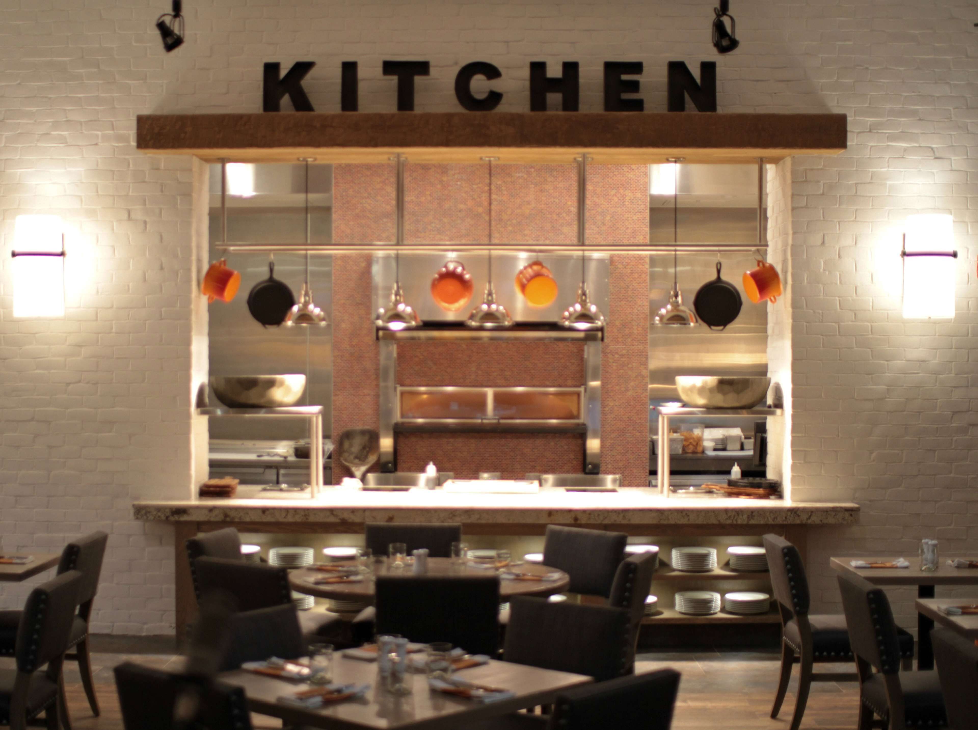 A modern kitchen with a brick wall, stainless steel appliances, and hanging pots.